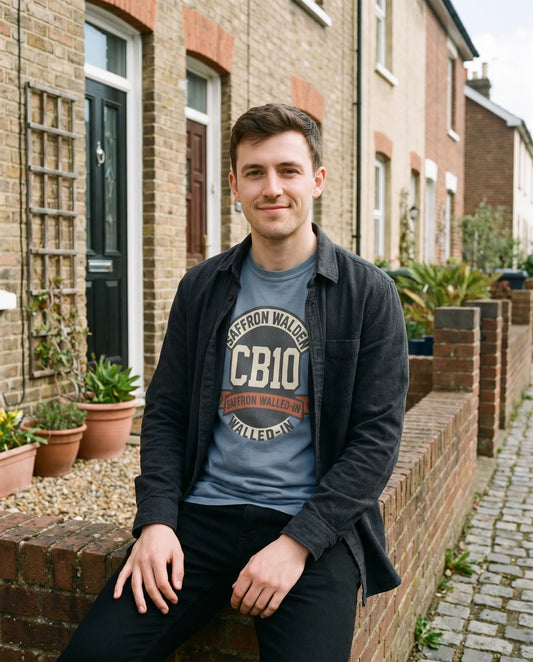 POSTCODE PRIDE CB10 tee in blue jean, worn under an open overshirt on a terraced street – WALLED IN Saffron Walden. AI-styled photo. Real product, printed to order.