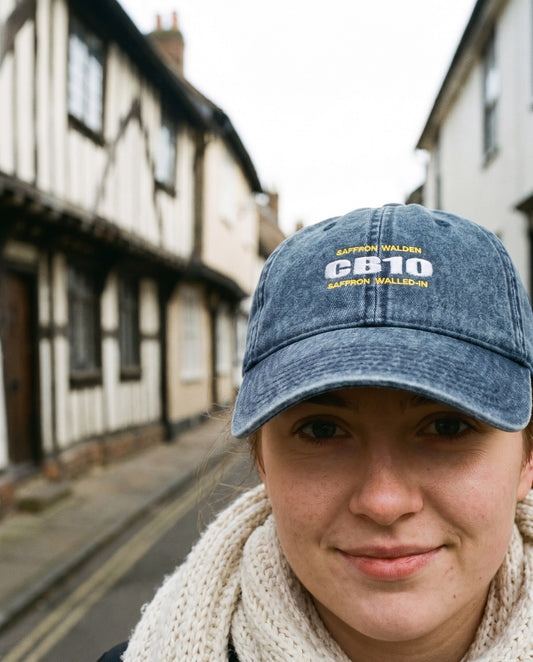 CB10 embroidered cap in washed denim, worn with a cream knit scarf on an old-town street – WALLED IN Saffron Walden. AI-styled photo. Real product, made to order.